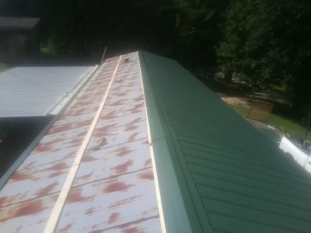 Old rusted panels beside newly installed green metal roofing — Wind Damage Roof Repair by Roofing Brothers in Spencerville