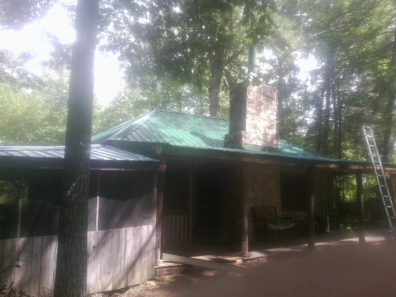 Green metal roof and stone chimney above a log cabin porch in Spencerville